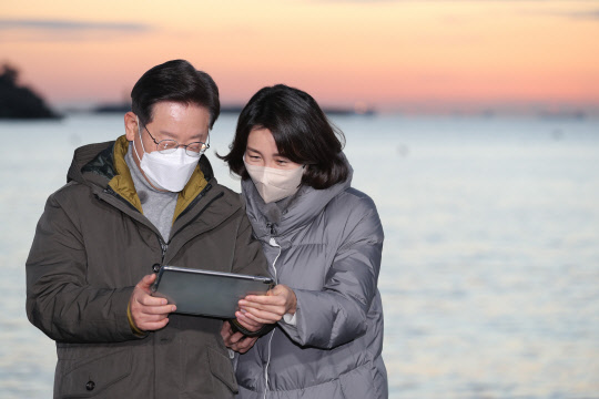 지난 1월2일 이재명(왼쪽) 더불어민주당 대선후보가 부산시 사하구 다대포해수욕장에서 부인 김혜경 씨와 함께 '2022 글로벌 해돋이 : 지구 한 바퀴' 온라인 해맞이 행사에서 유튜브 생중계를 보고 있다.[연합뉴스]